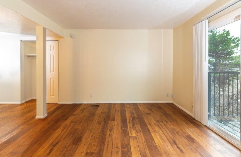 Empty room with hardwood floors, beige walls, sliding glass door leading to balcony, and a closet.