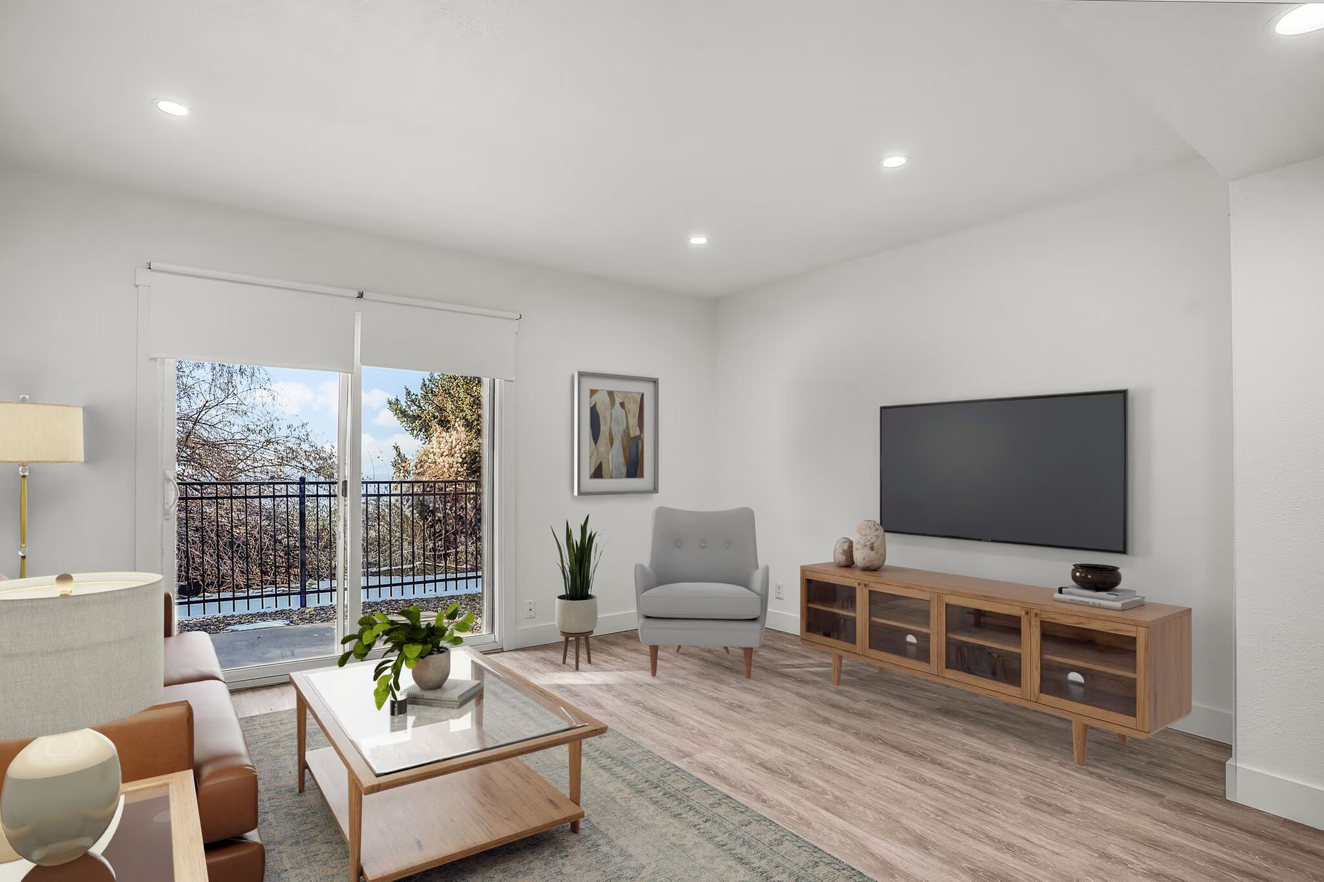 Living room with TV, sliding door to balcony, gray chair, wood floor, and light wood entertainment center.