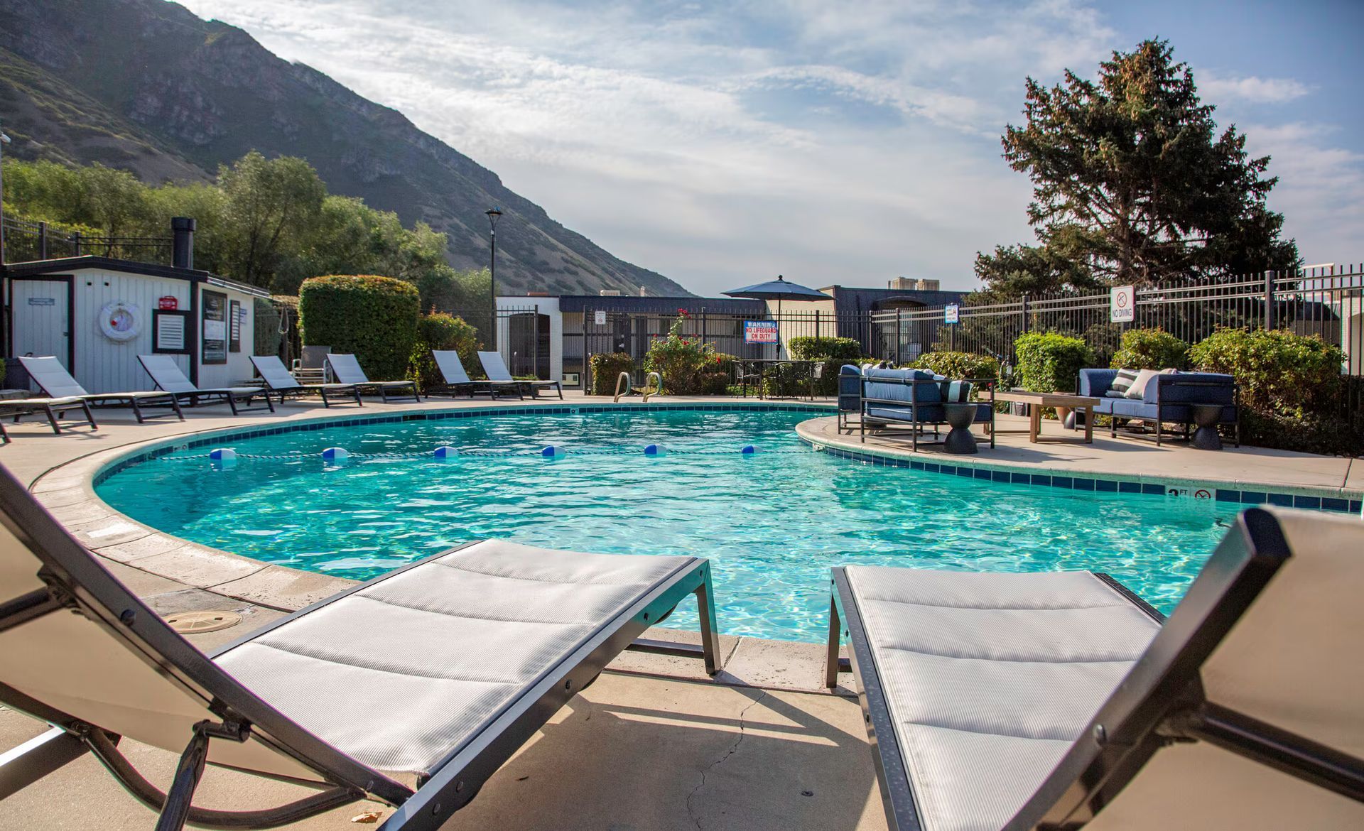 Swimming pool with lounge chairs, mountain backdrop, sunny day.