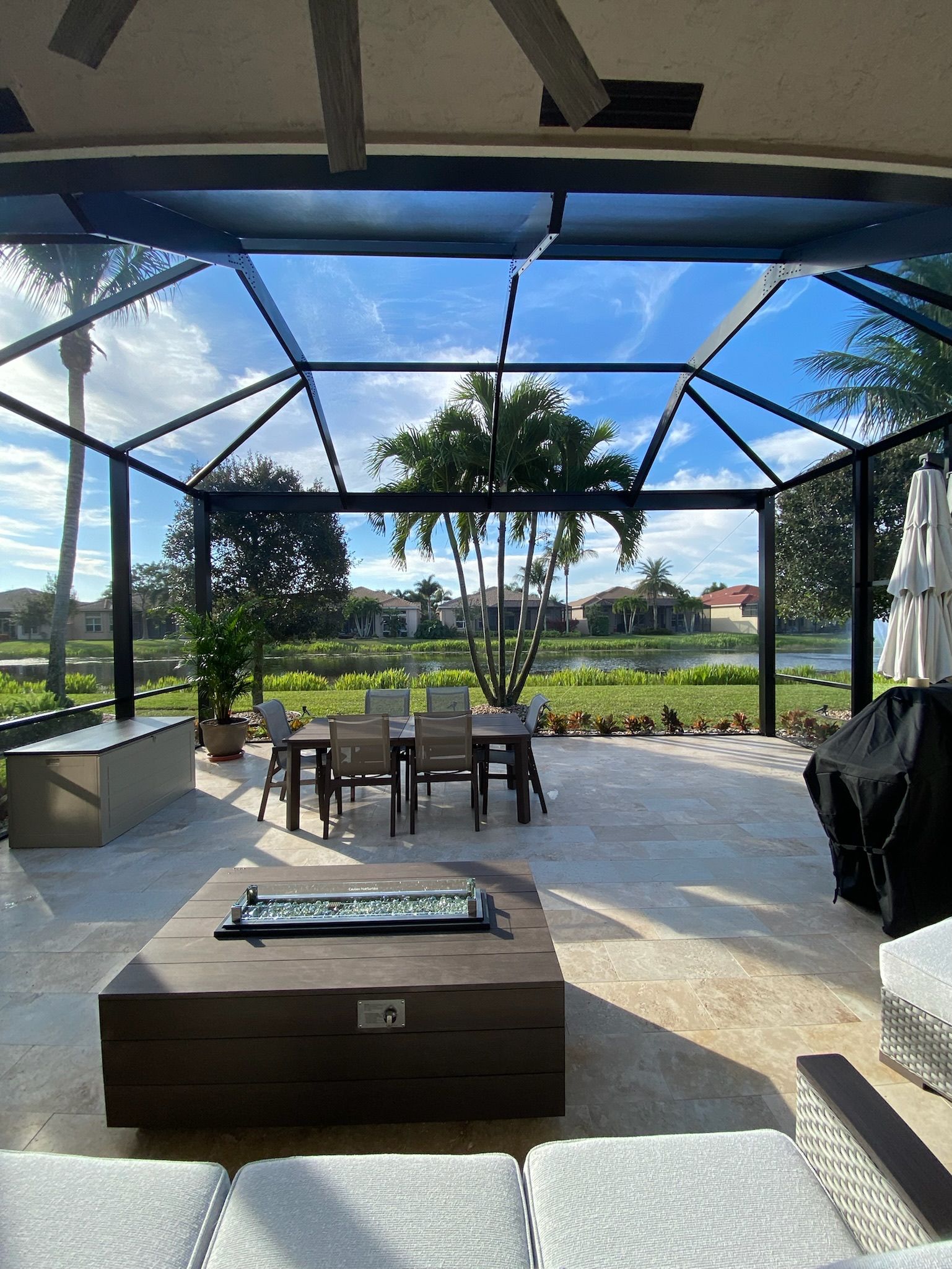 Covered patio with seating area, patterned rug, and a view of the pool and palm trees beyond