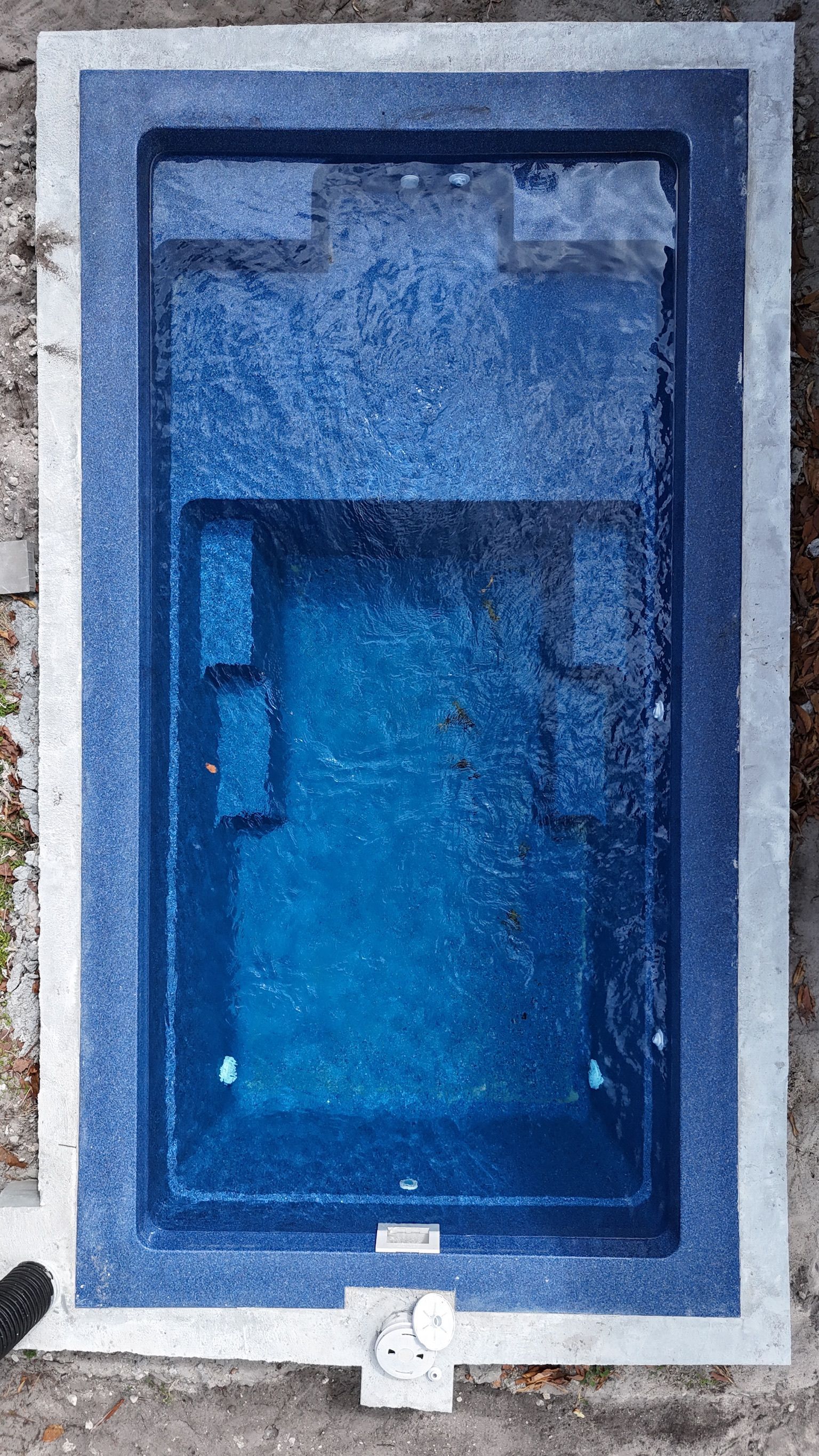 Blue-tinted rectangular pool seen from above with a small white fixture at the bottom edge