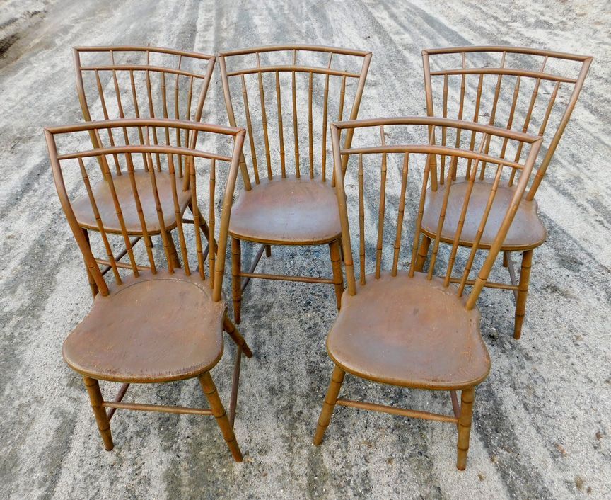 Five wooden chairs with curved backs and tan seats arranged on a concrete surface.
