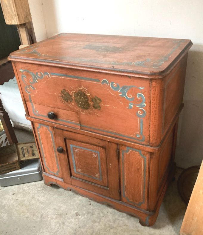 Vintage red-painted wooden cabinet with decorative trim and floral accents on a concrete floor