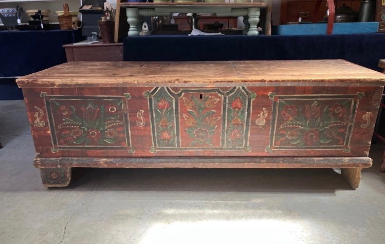 Large painted wooden chest with red floral panels in a museum or shop setting