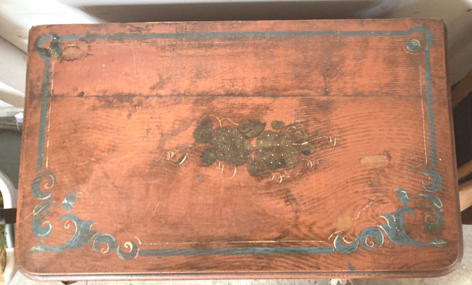 Vintage red-painted wooden cabinet with decorative trim and floral accents on a concrete floor