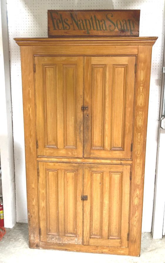 Wooden cabinet with two paneled doors and a sign on top, standing against a wall