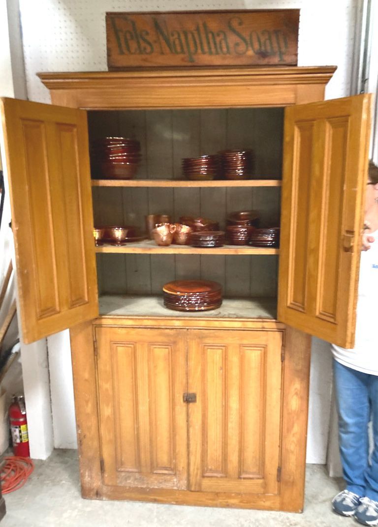 Wooden cabinet with two paneled doors and a sign on top, standing against a wall