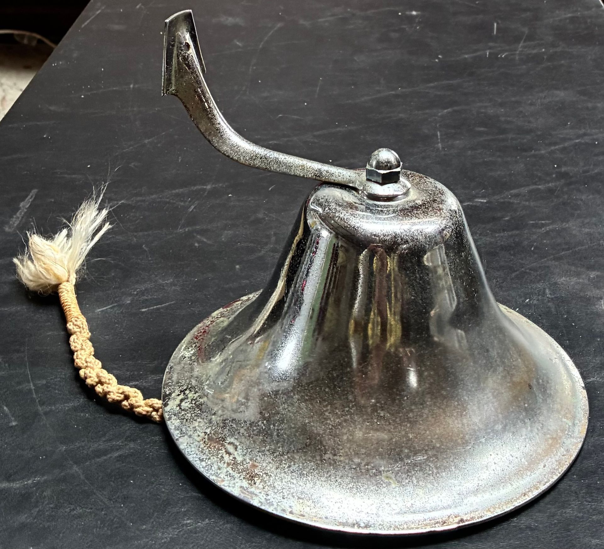 Vintage brass hand bell with a braided cord on a dark surface