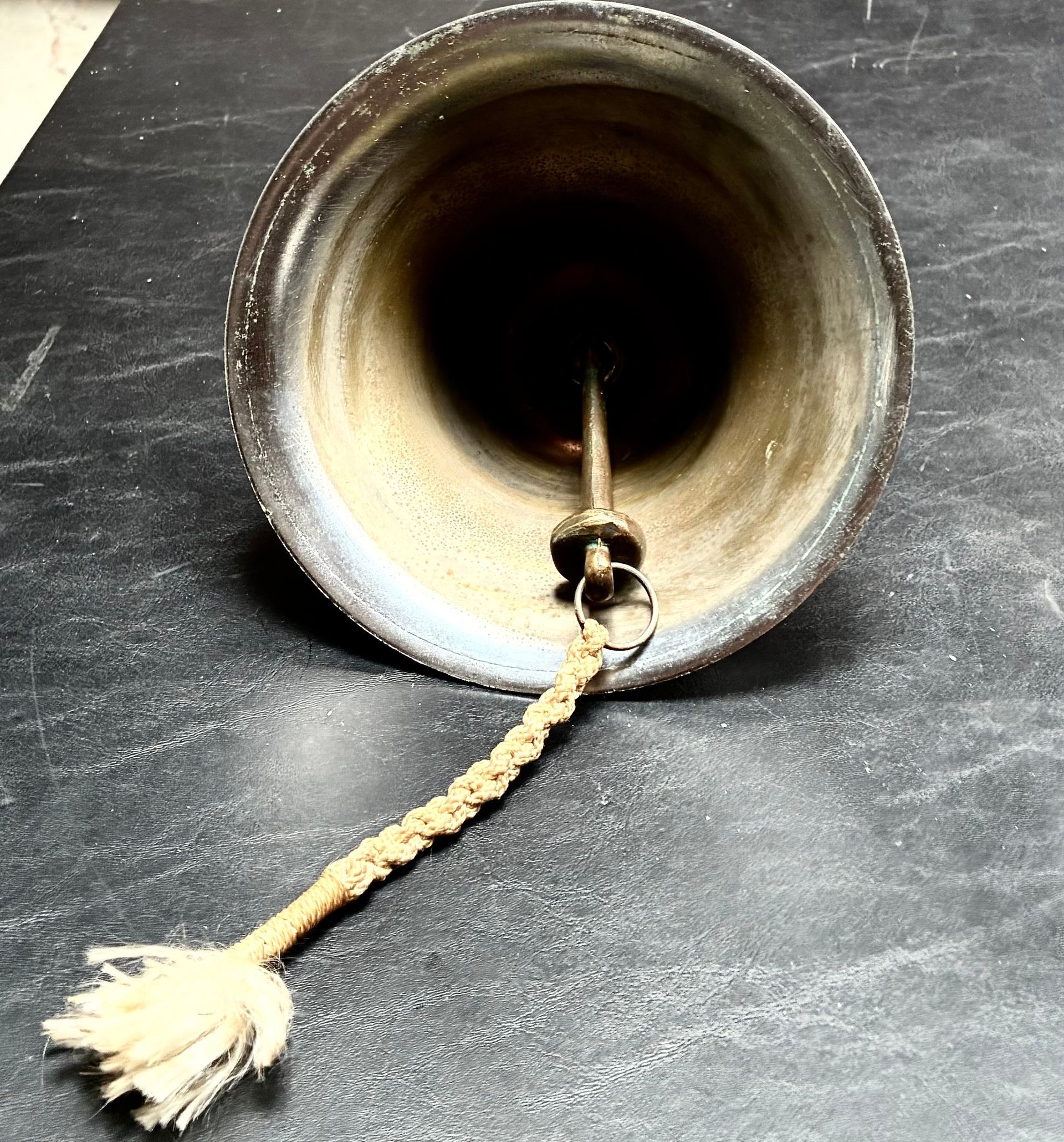 Vintage brass hand bell with a braided cord on a dark surface