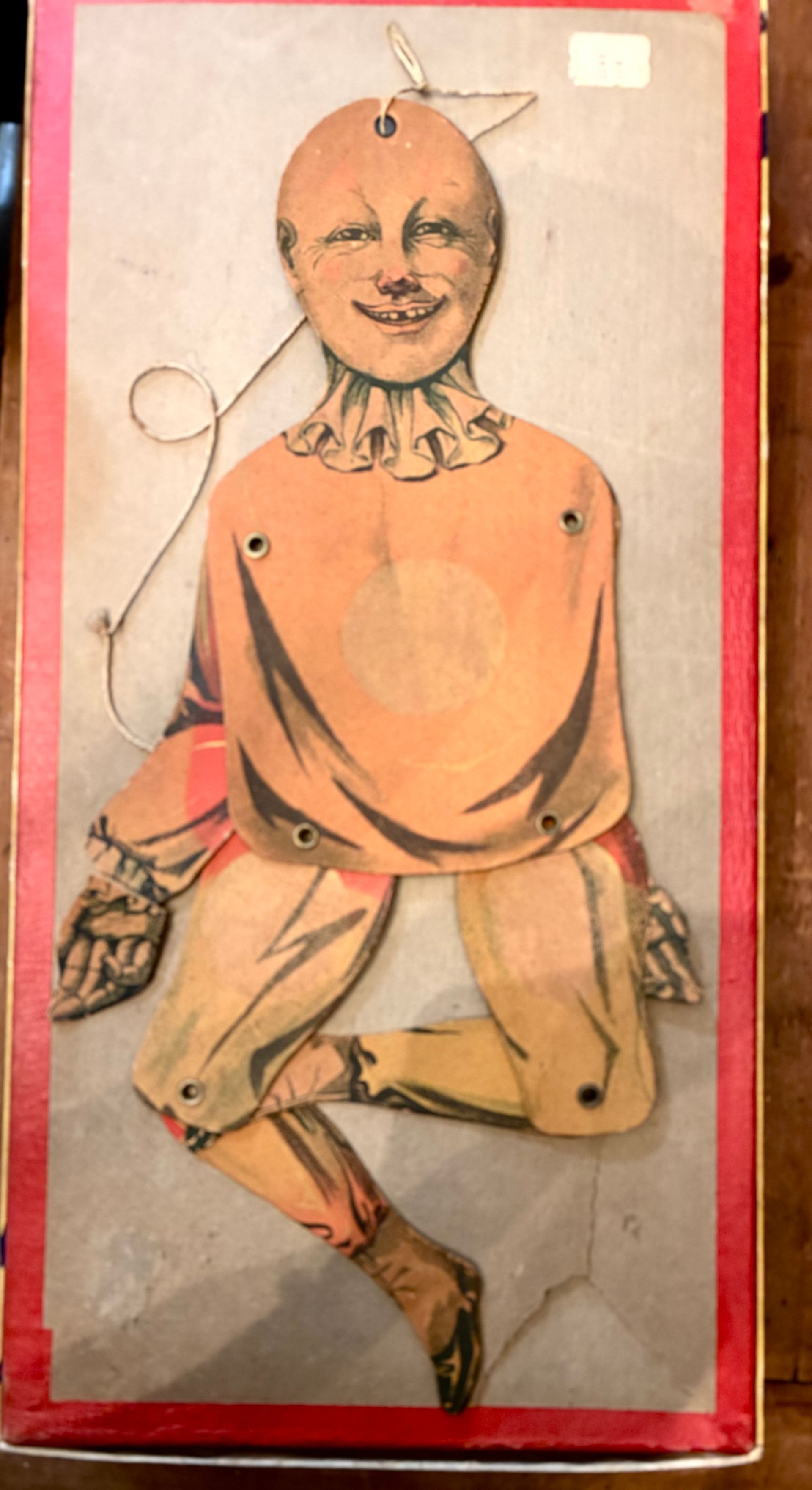 Illustrated cutout figure in an orange robe on a white background with a red border, holding a rope-like line