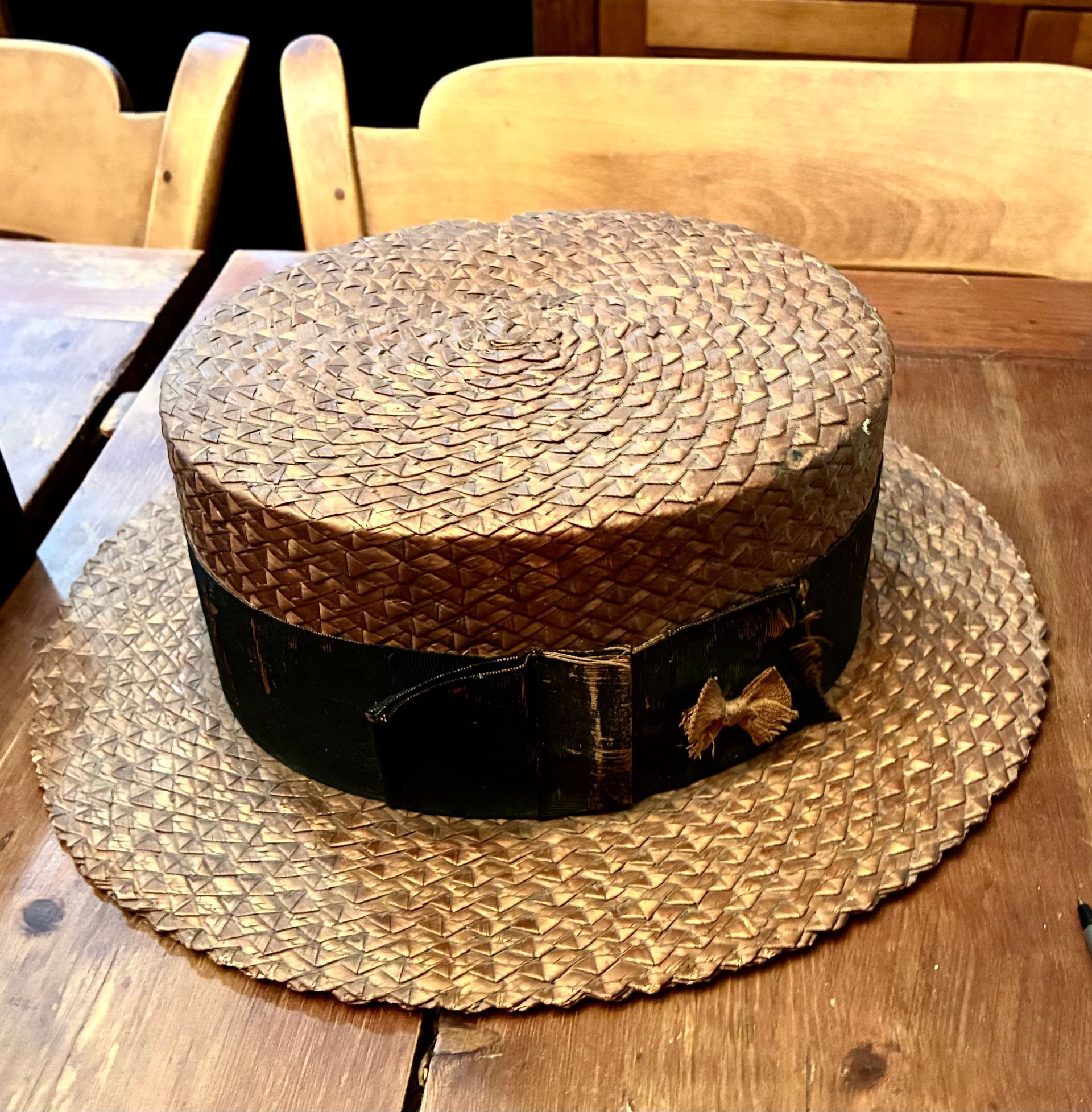 Round woven straw hat with a black band resting on a matching straw placemat on a wooden table.