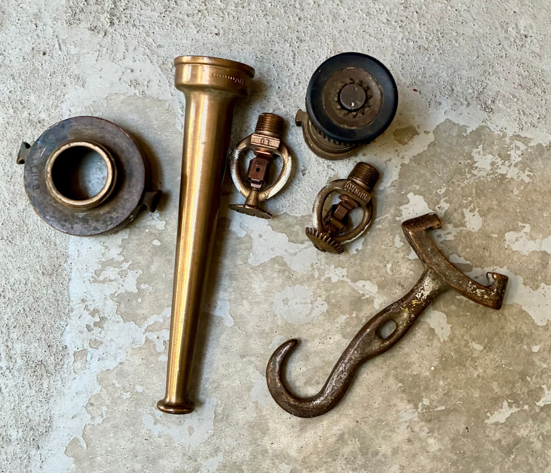 Assorted brass and metal faucet and plumbing parts laid out on a worn concrete surface