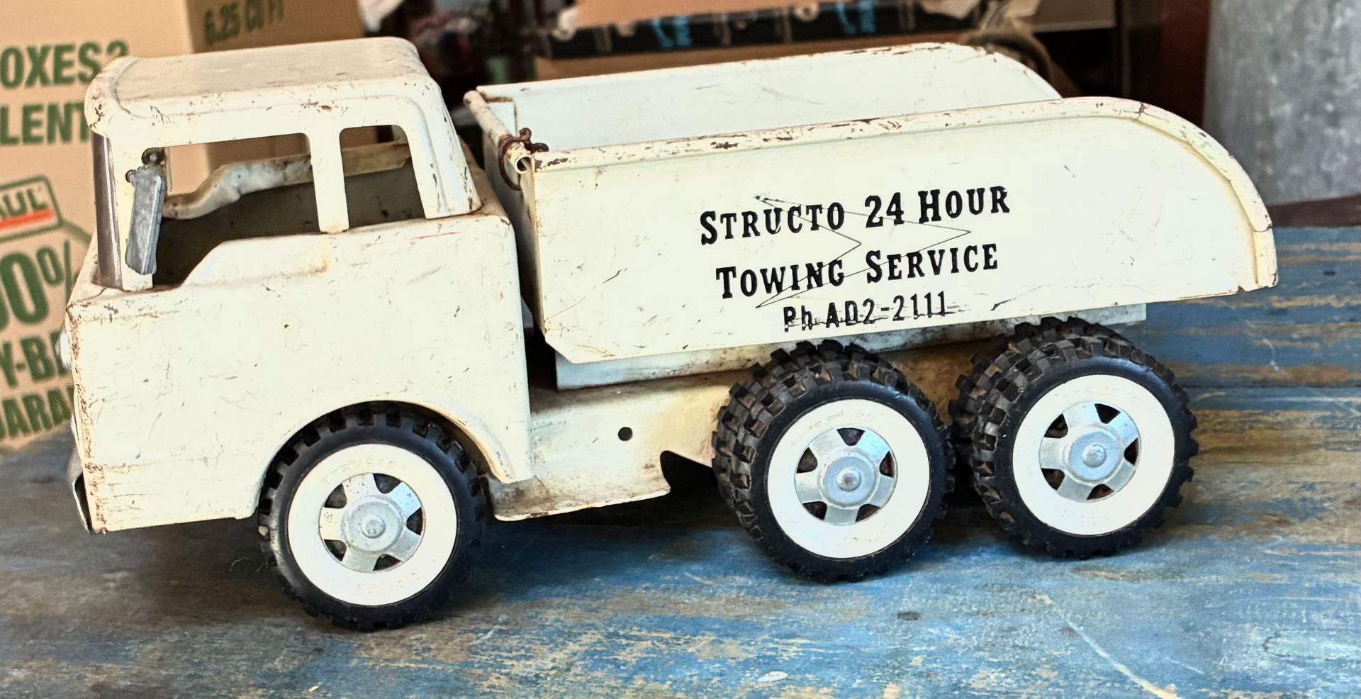 Vintage white toy tow truck with six blue wheels and “24 Hour Towing Service” text.