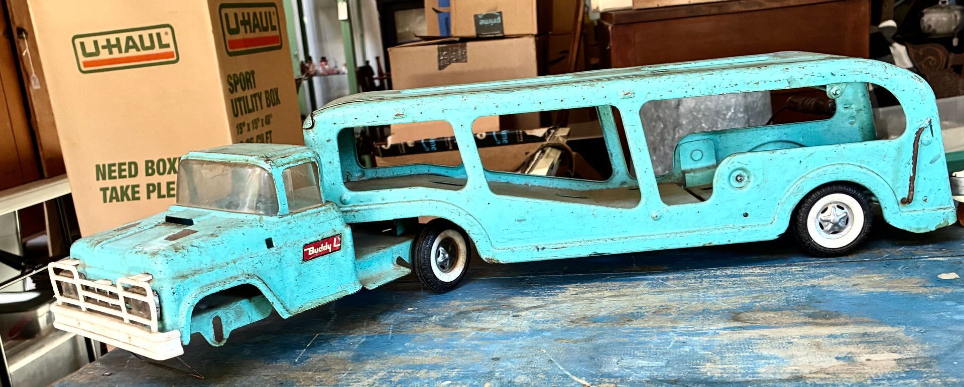 Turquoise toy truck hauling a matching camper trailer on a tabletop in a garage-like setting
