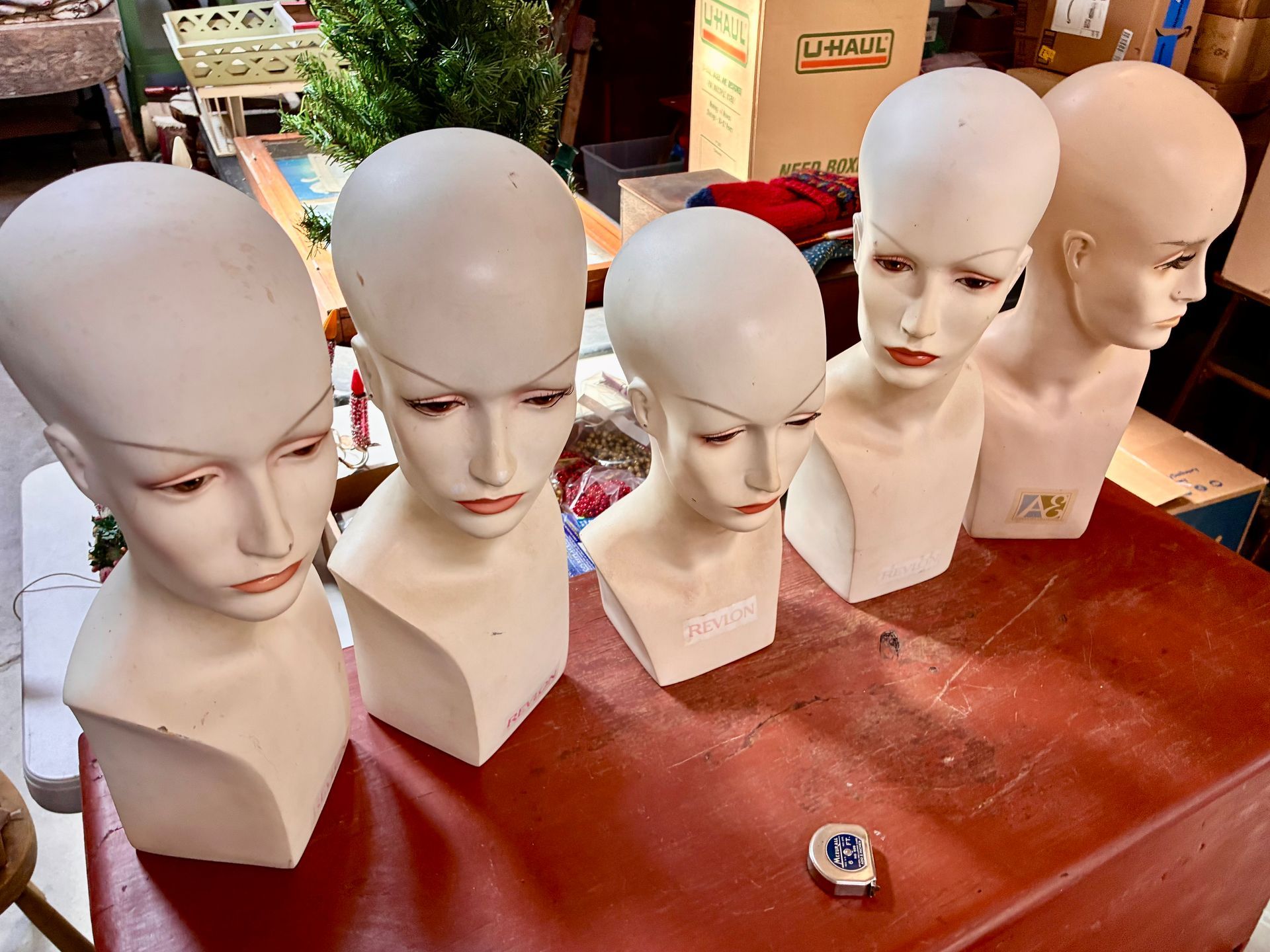 Five bald mannequin heads on a table in an outdoor market stall