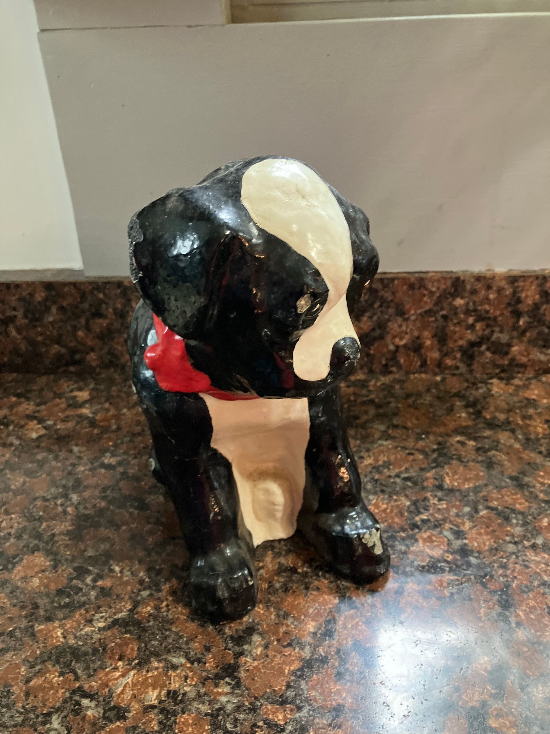 Small black-and-white dog figurine with a red collar on a speckled countertop