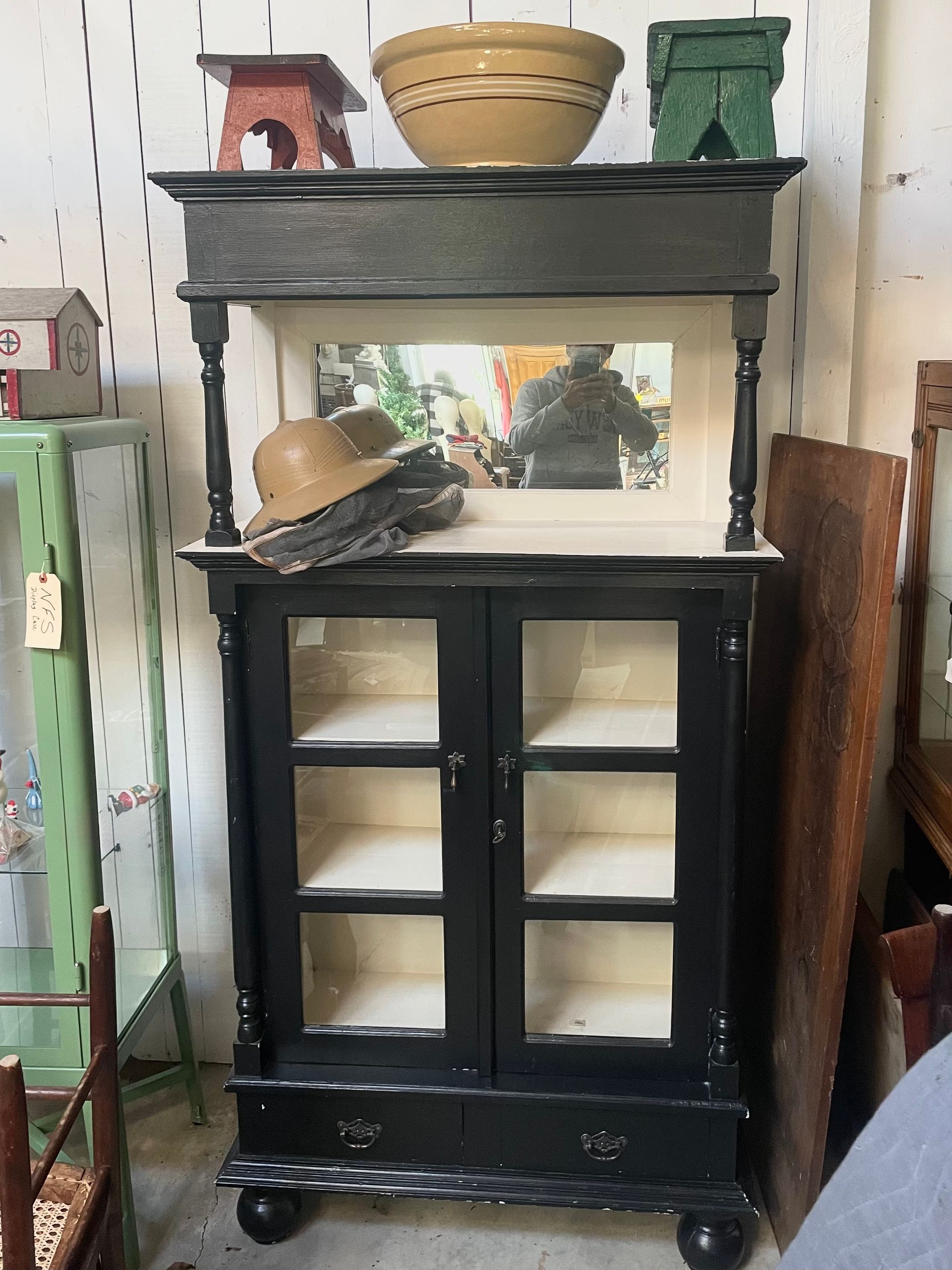 Black cabinet with glass doors, shelf decor, and a mirror on top in a shop setting