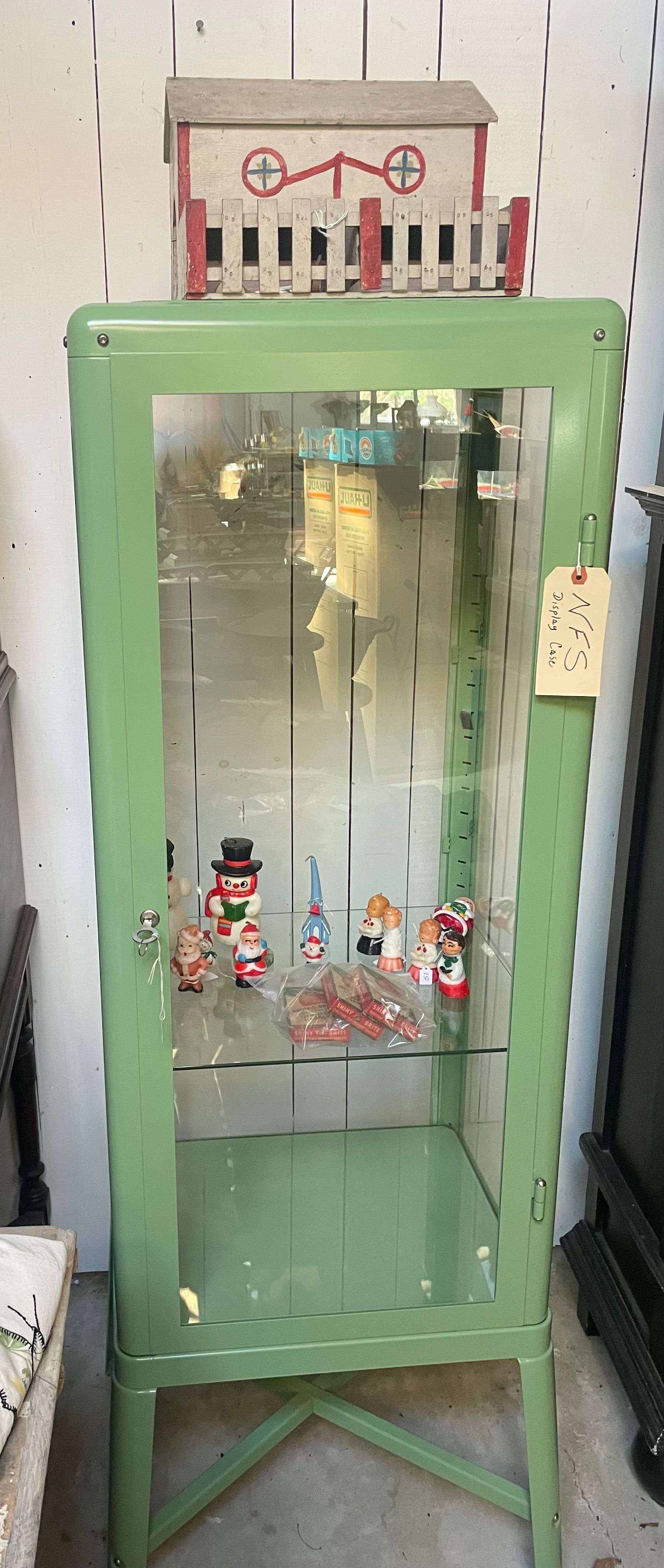Mint-green glass display cabinet with dishes inside, in a cluttered room