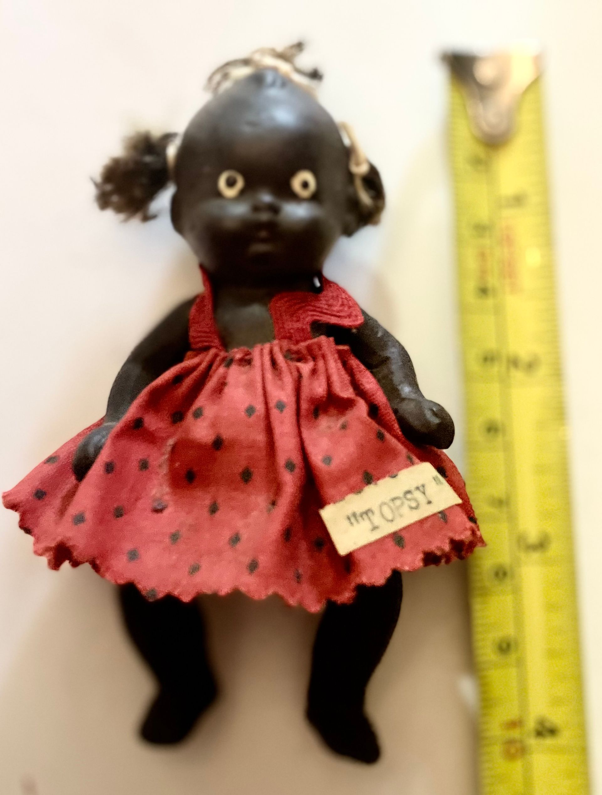Small black doll in a red polka-dot dress beside a yellow ruler