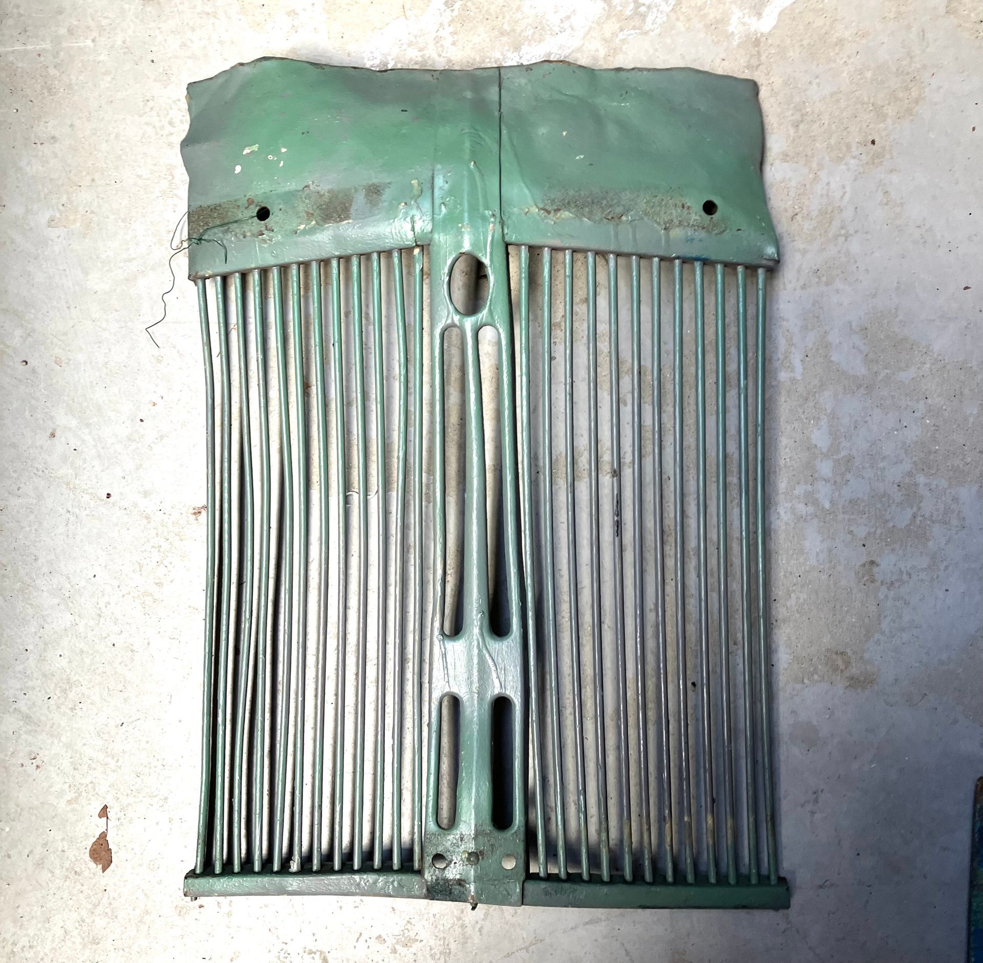 Green metal vent grate with vertical slats on a concrete surface