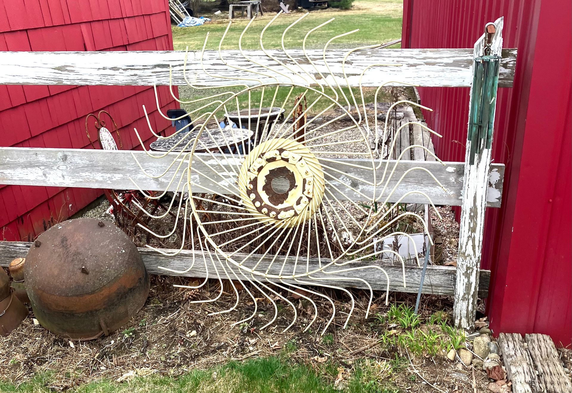 Spiderweb-covered wheel mounted on a white fence beside red barns and a rusty metal object