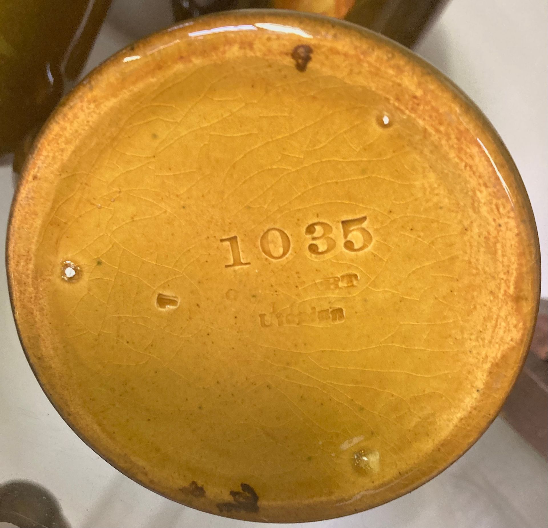 Bottom of a yellow ceramic object with the number 1035 stamped in the center.