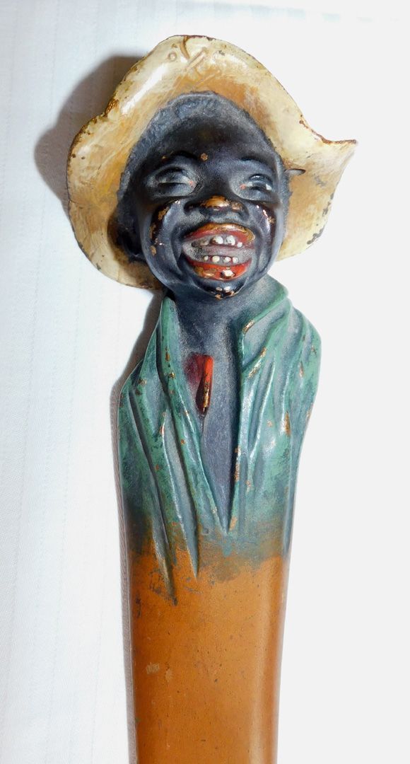 Small painted figurine with a straw hat, dark face, green jacket, and orange body.