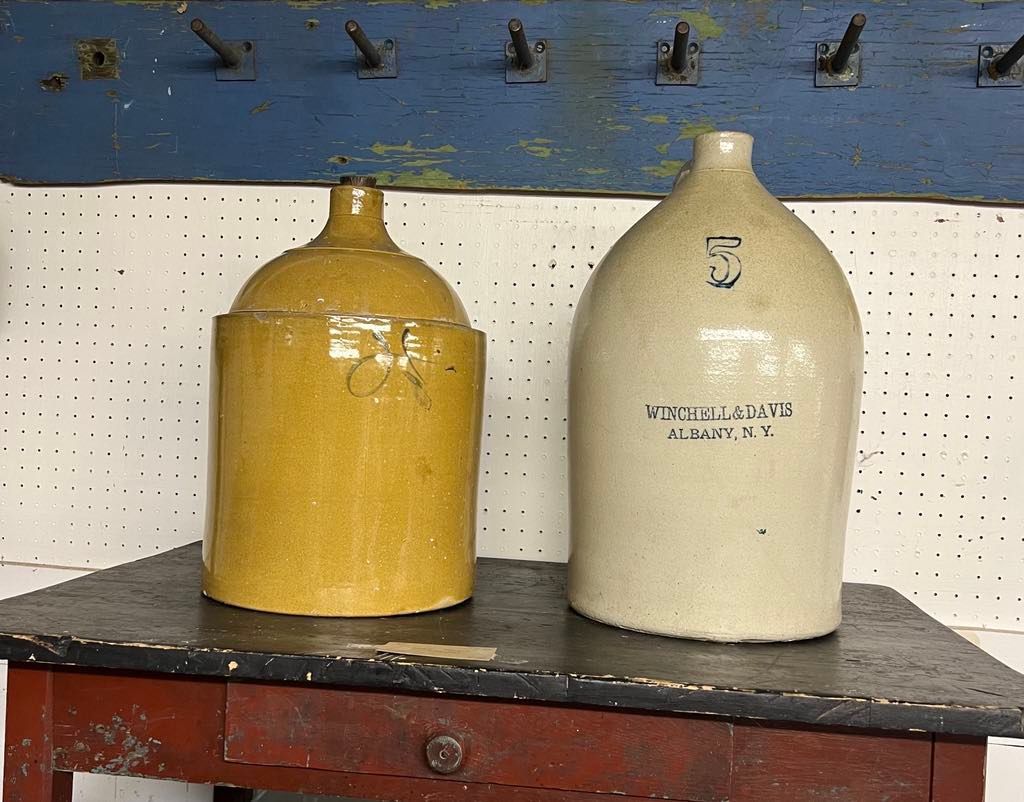 Two ceramic jugs, one yellow and one cream, on a tabletop against a pegboard wall.