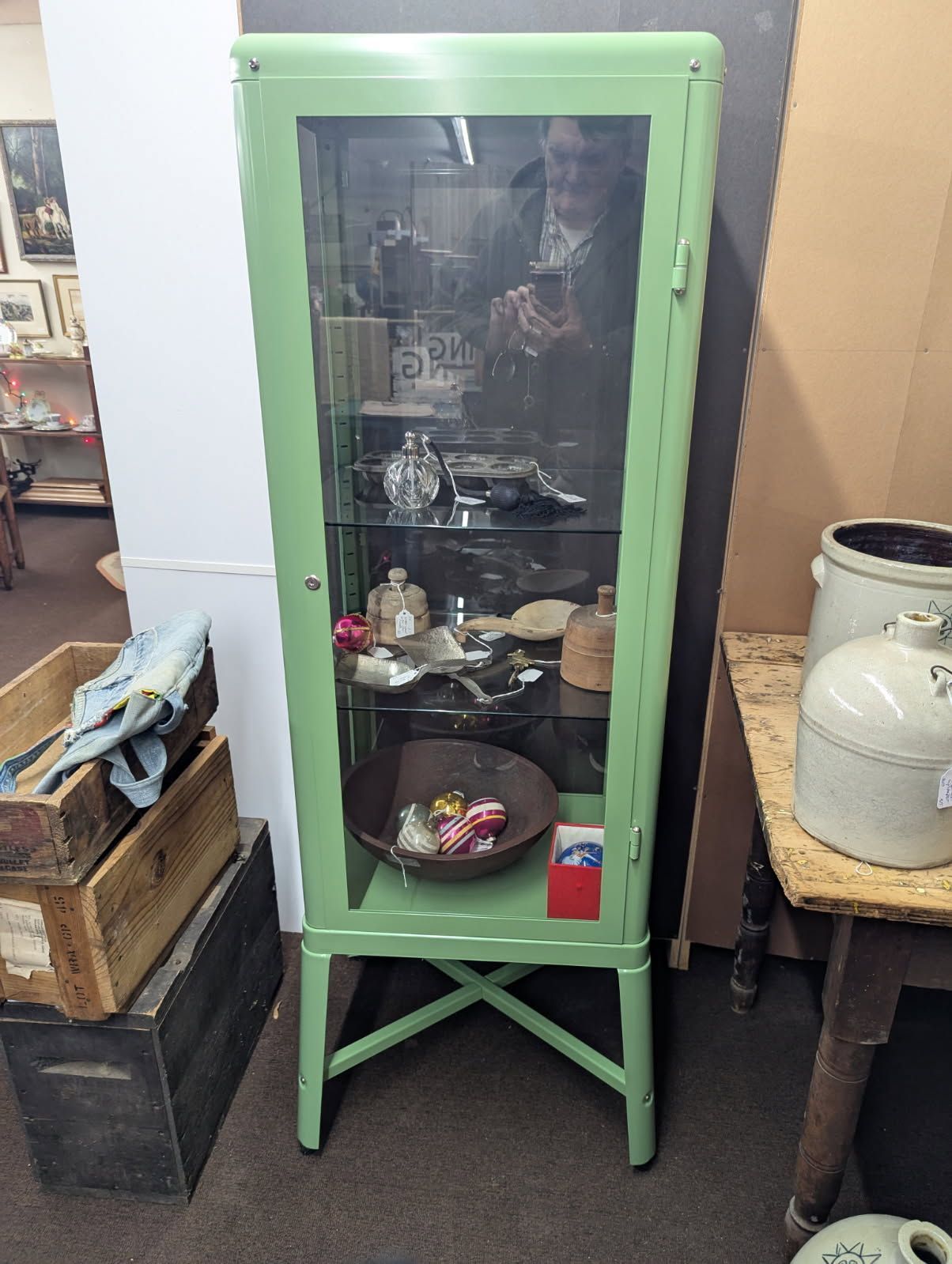 Mint-green glass display cabinet with dishes inside, in a cluttered room