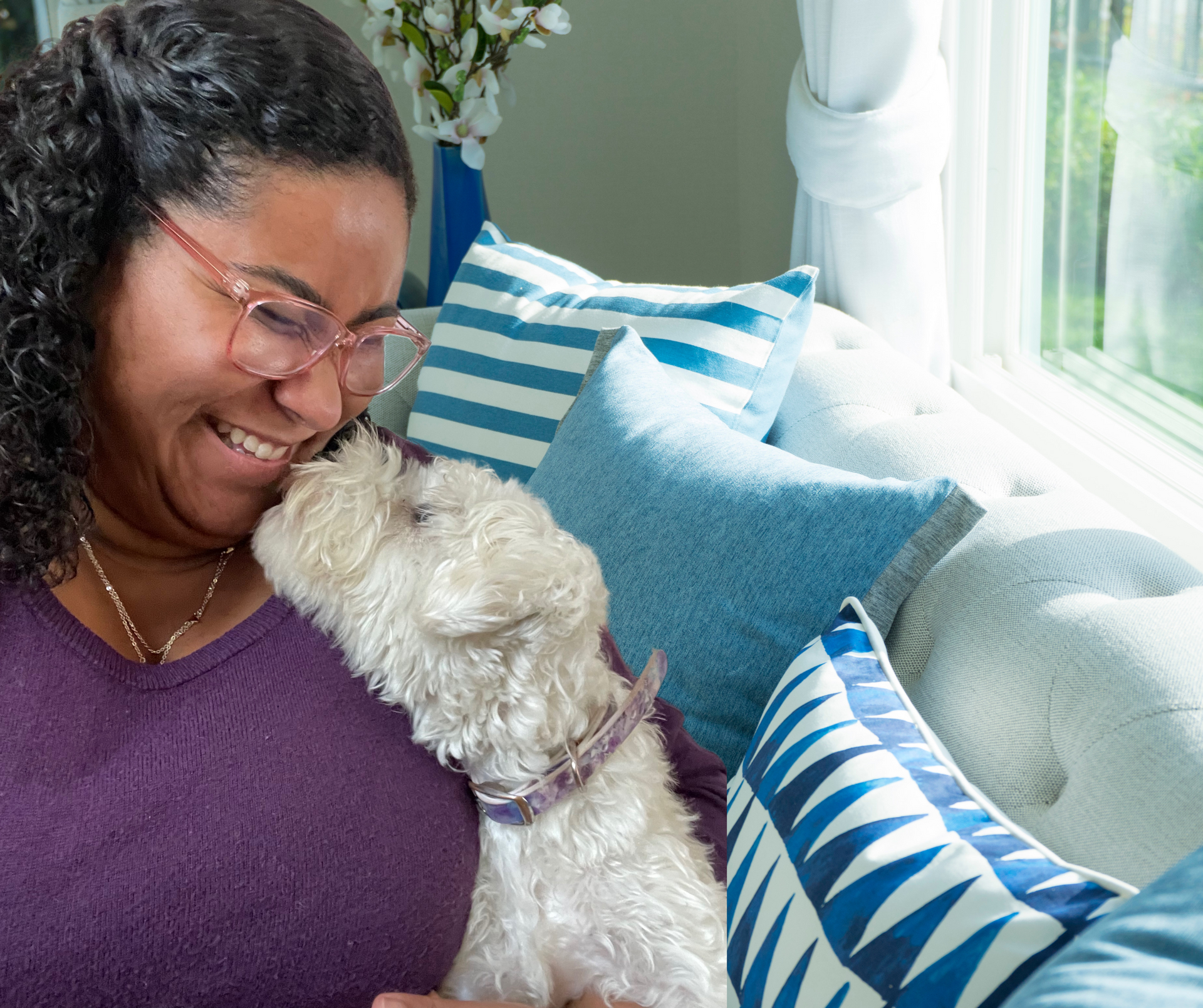 A woman is sitting on a couch holding a small white dog.