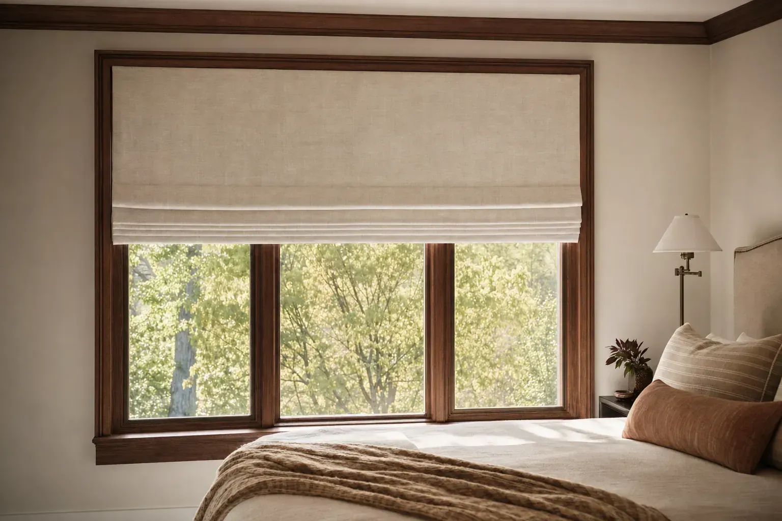 Bright bedroom with a white bed, tufted bench, and woven Roman shades over a large window. Bright bedroom with a white bed, tufted bench, and woven Roman shades over a large window.
