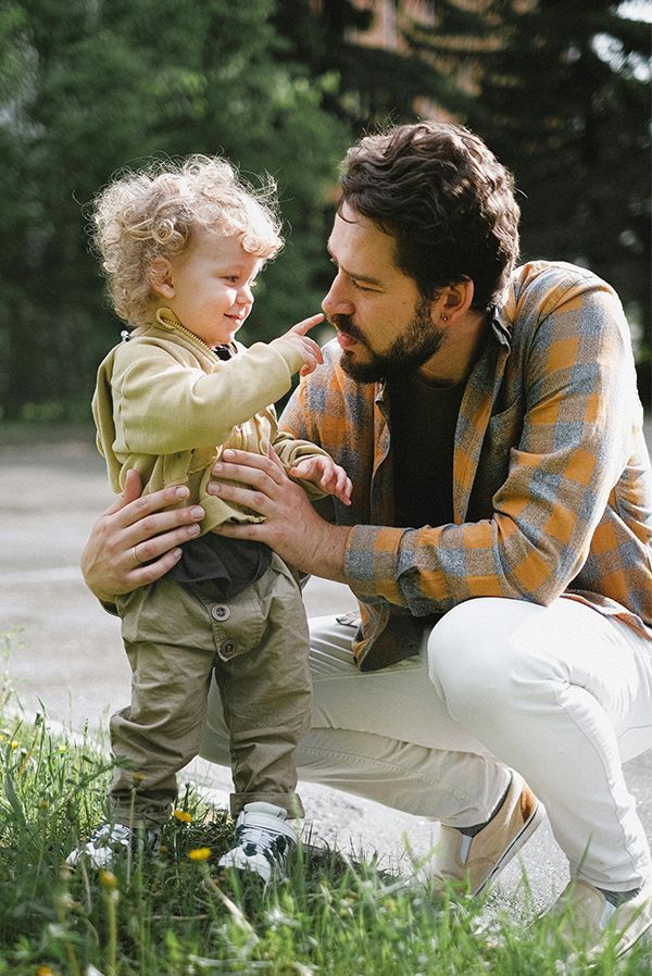 Adult kneels beside toddler in a grassy field, smiling as they touch noses.
