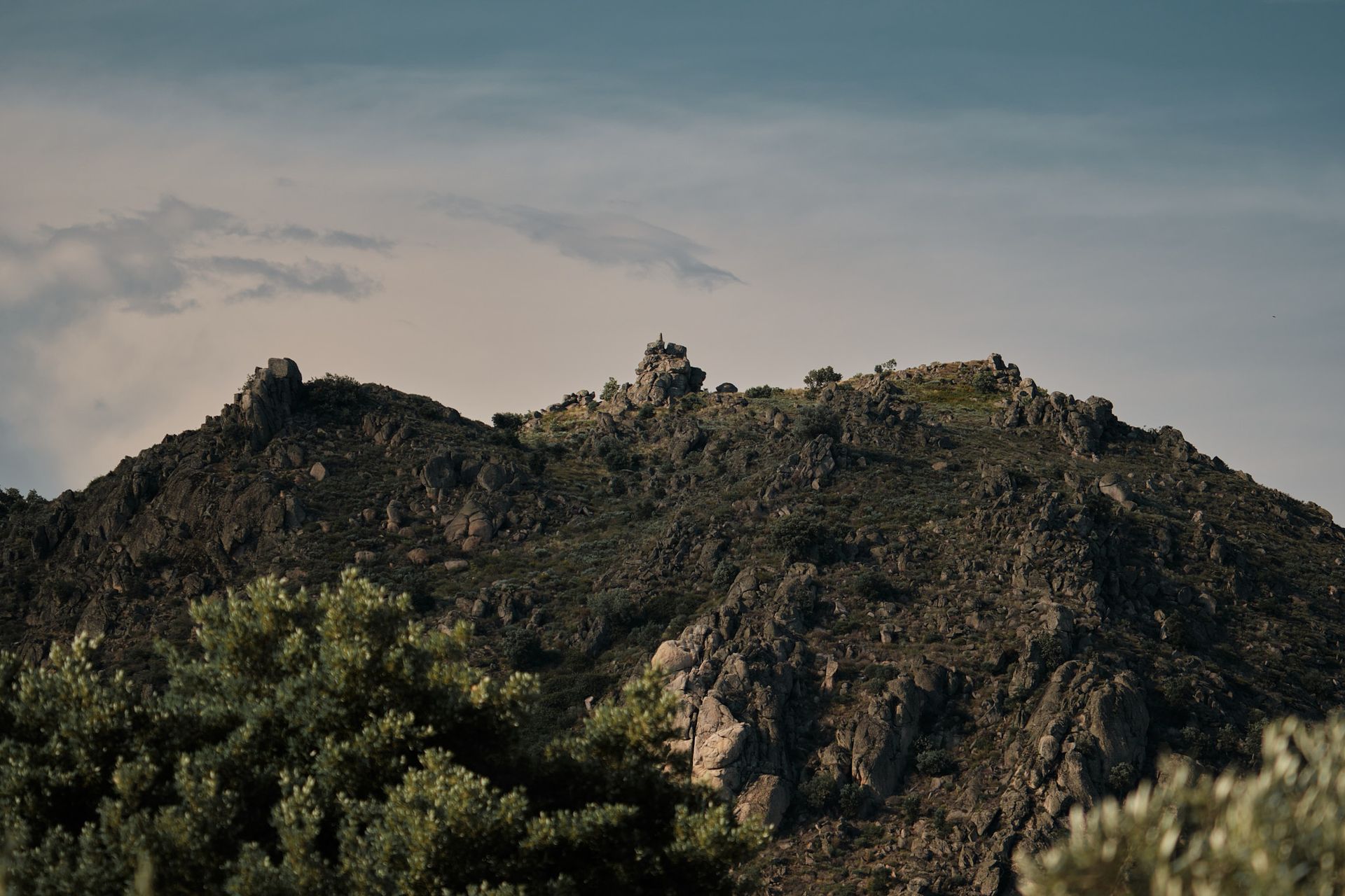 A mountain covered in trees and rocks with a blue sky in the background