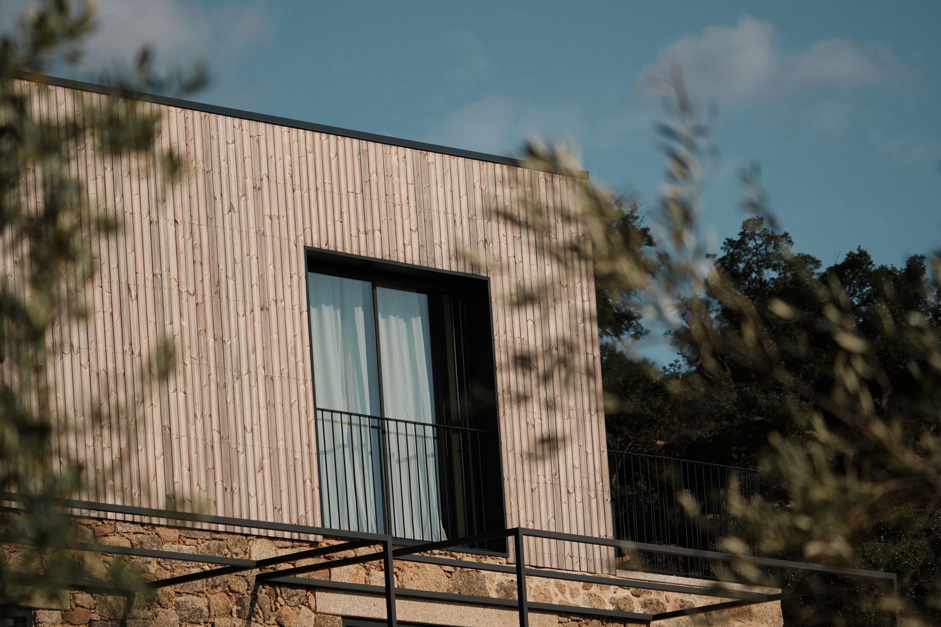 A house with a balcony and a large window is surrounded by trees.