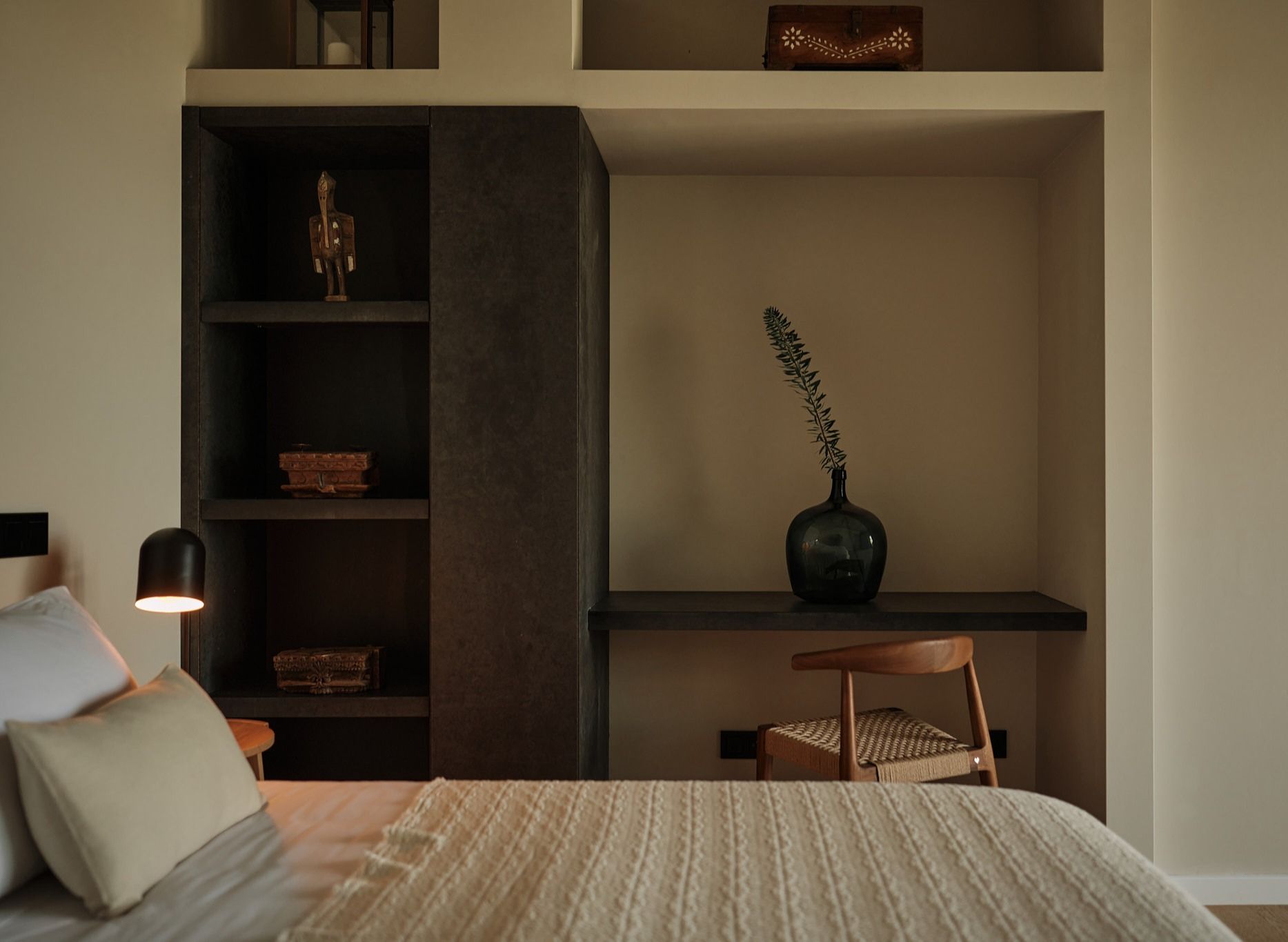 A bedroom with a bed and a desk with a vase on it