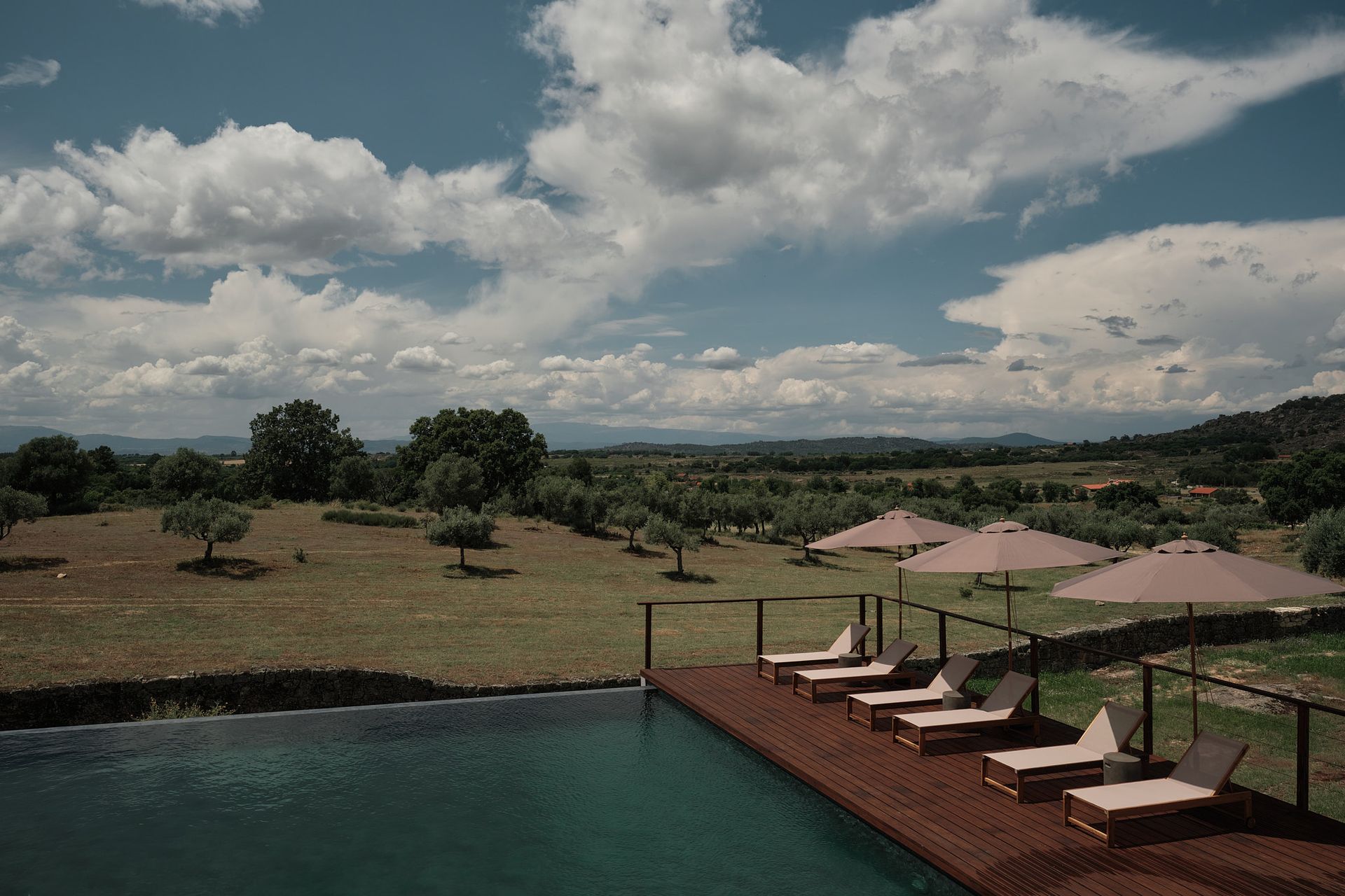 A swimming pool surrounded by chairs and umbrellas in the middle of a field.