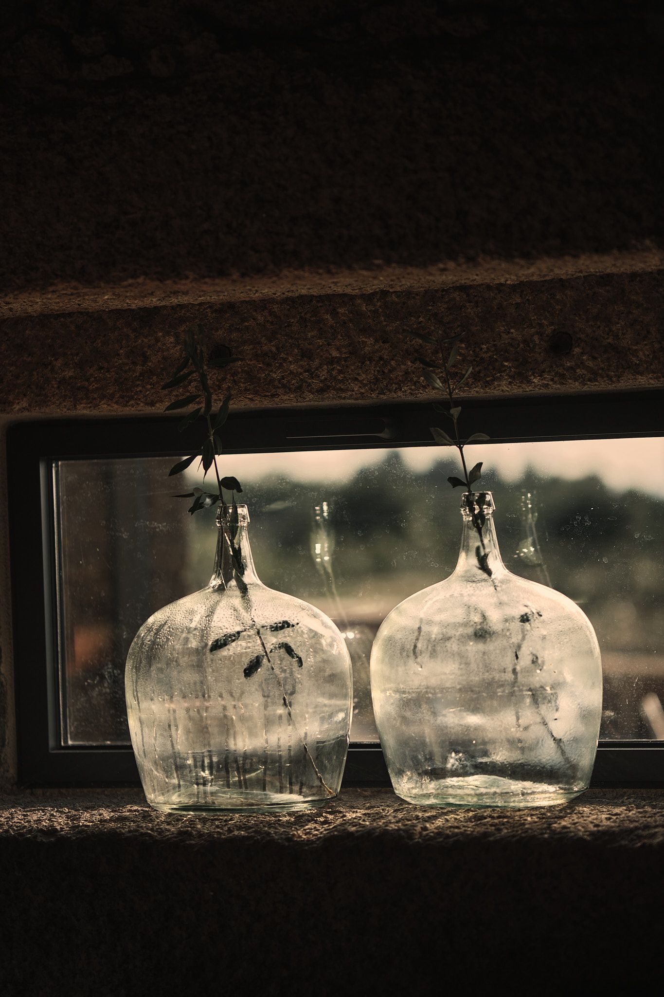 Two empty bottles are sitting on a window sill.