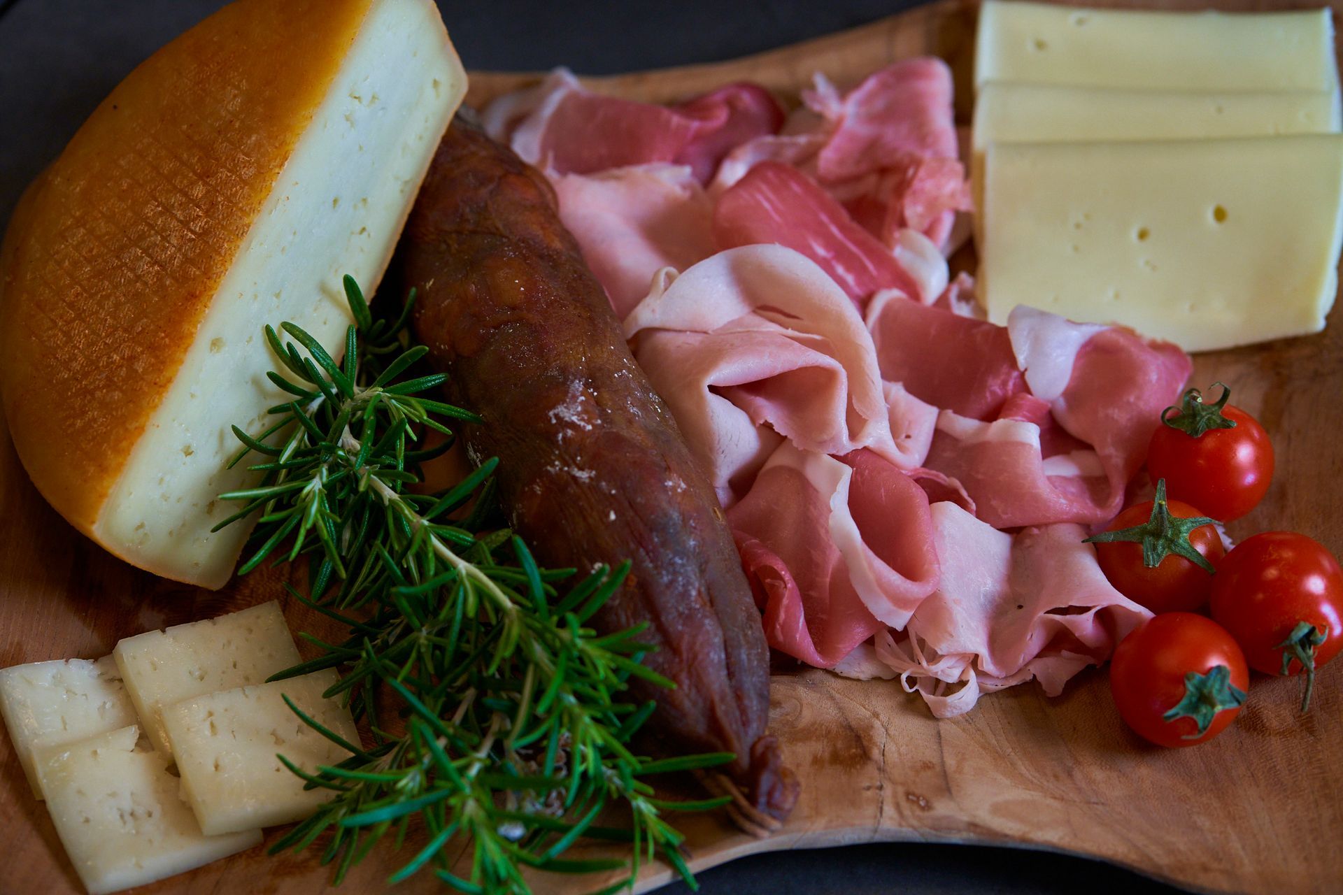 A wooden cutting board topped with meat , cheese , tomatoes and bread.
