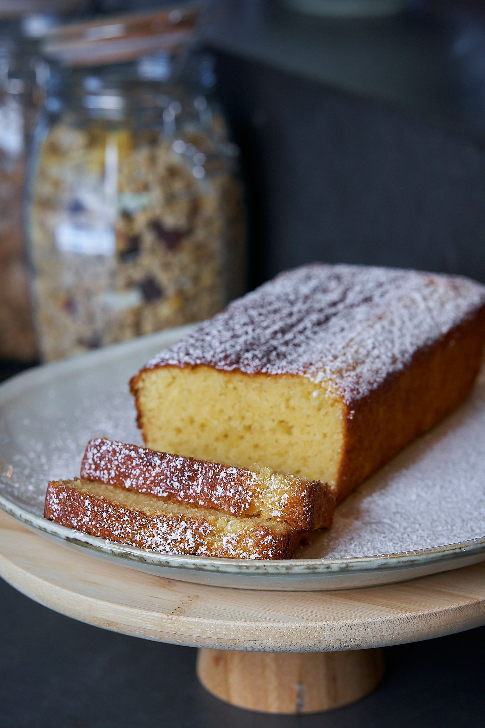 A loaf of cake with powdered sugar on top is on a plate.