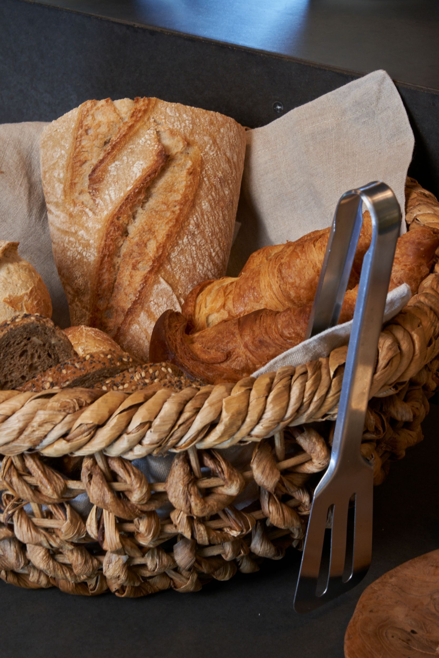 A basket filled with bread and tongs on a table.
