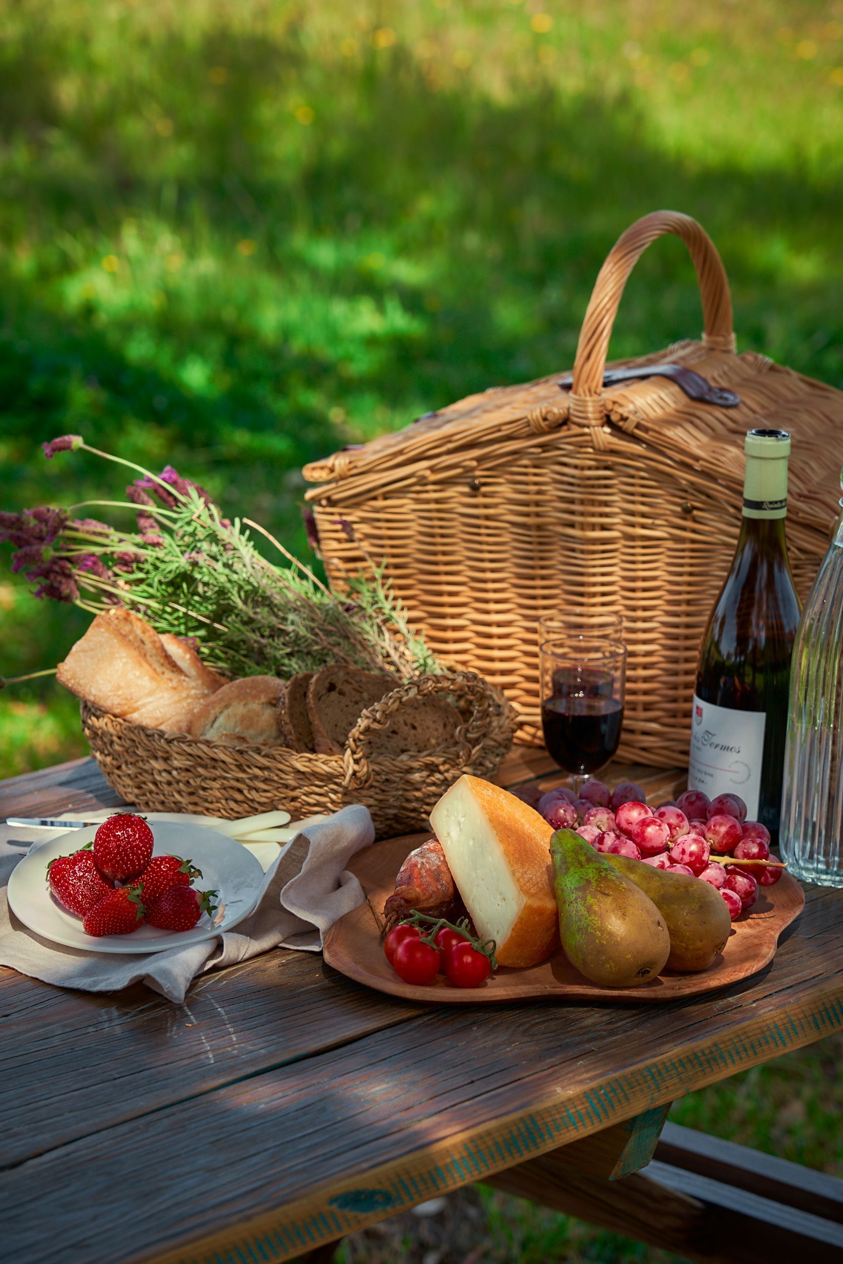 A picnic basket filled with food and wine is sitting on a wooden table.