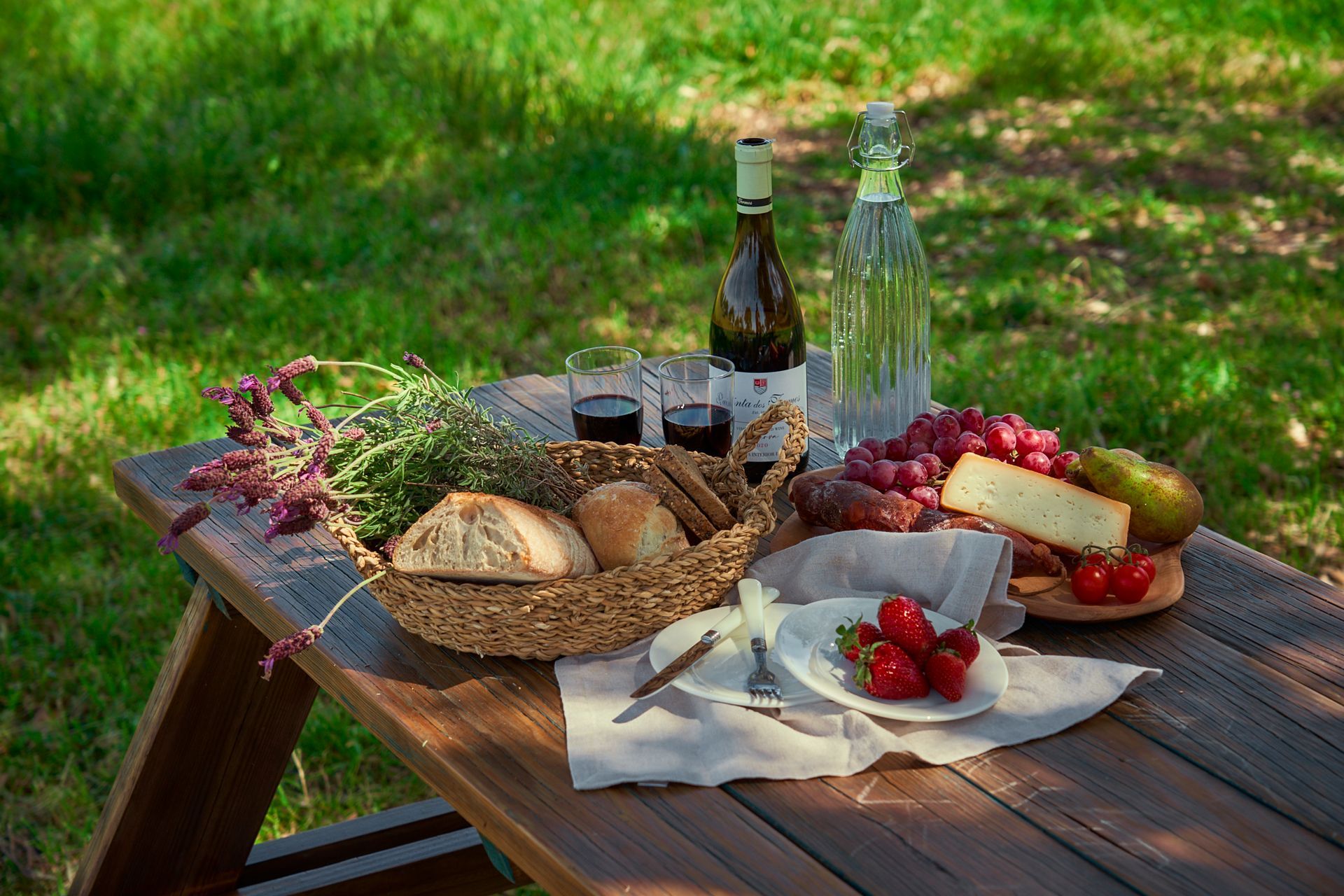 A wooden picnic table with food and wine on it.