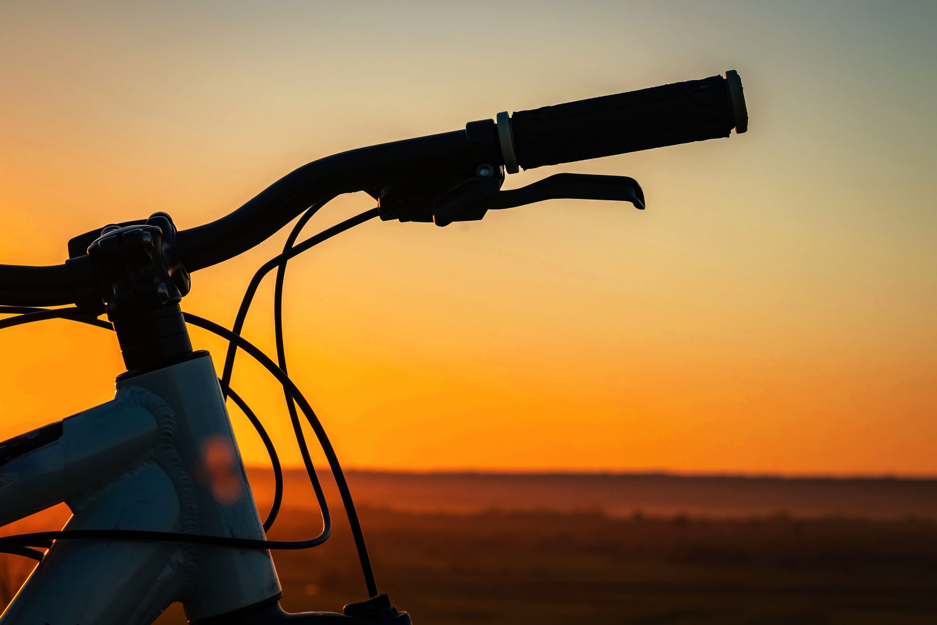 A close up of a bicycle handlebars with a sunset in the background.