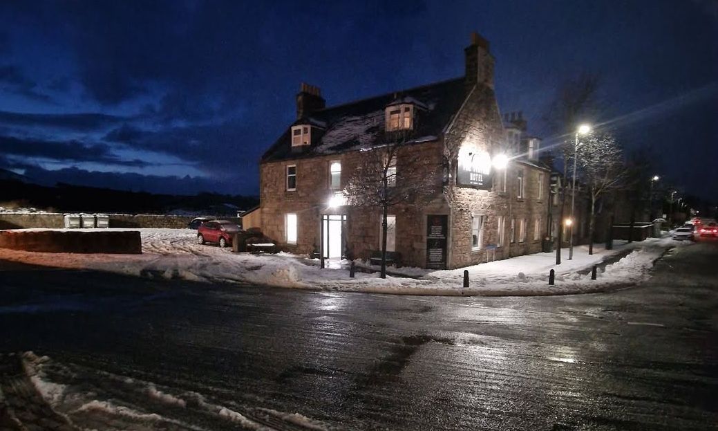 An old hotel in the dark with snow around and lights shining out