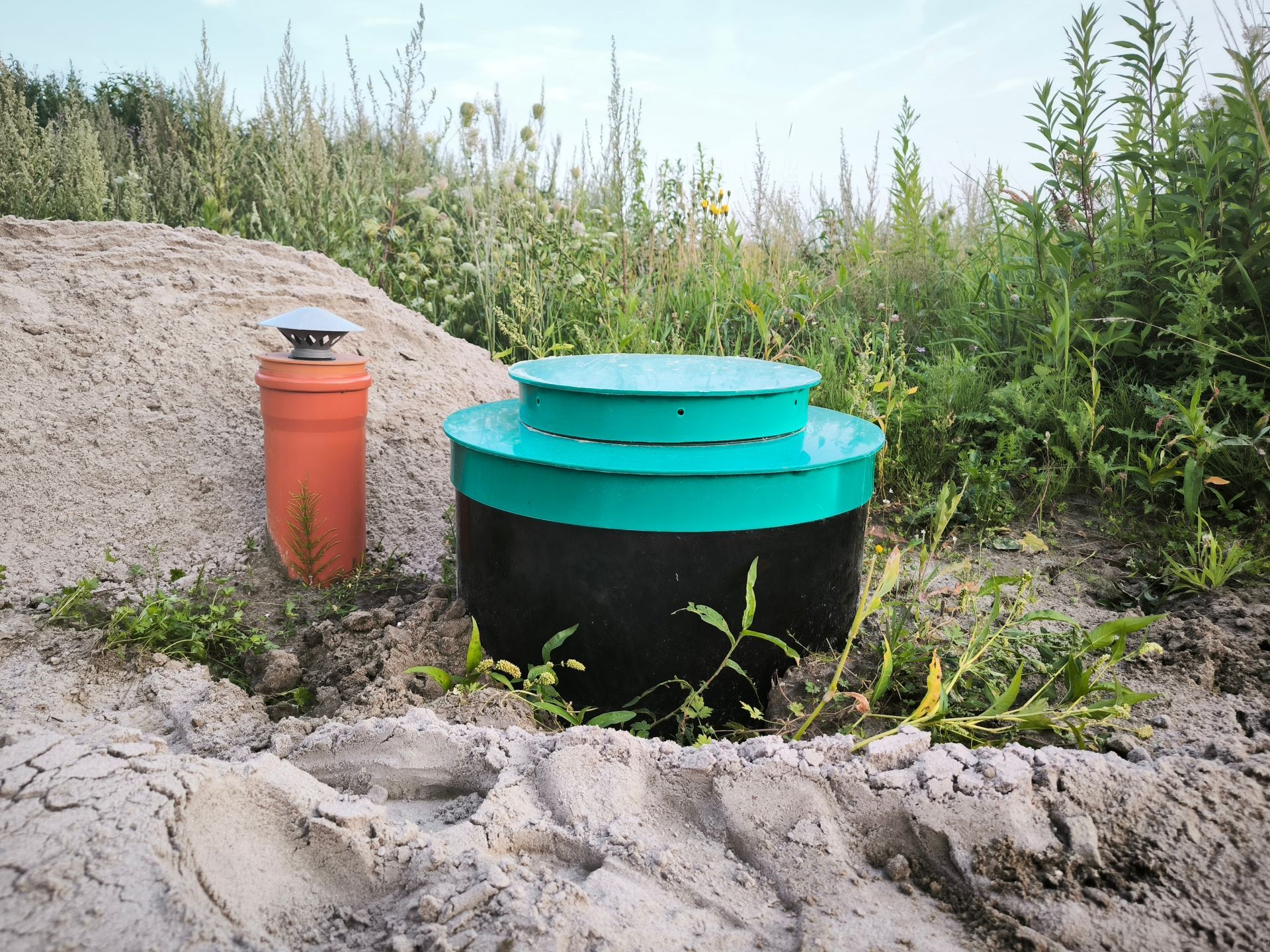 Septic tank with green risers and lids installed in sandy soil.