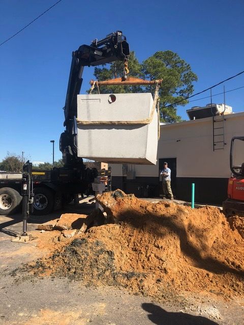 Excavator lifting a white dumpster over a dirt pile at a construction site under a clear blue sky