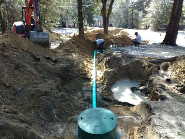 Workers installing a blue pipe in a dug trench at a wooded construction site
