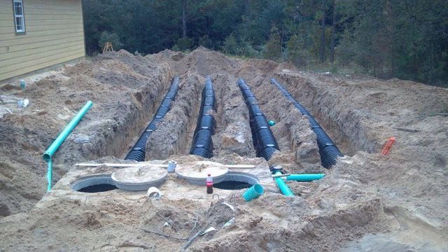 Excavation site with blue drainage pipes laid in trenches and a septic tank in the foreground