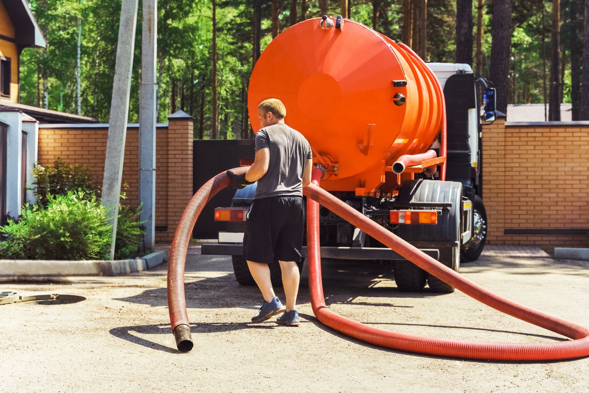 Worker handling large hose near orange vacuum truck in outdoor setting.