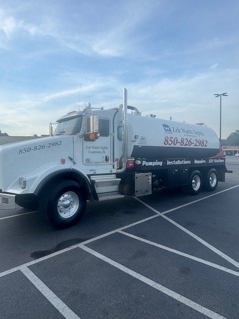 White septic tank truck in a parking lot; company name with phone number on the side.